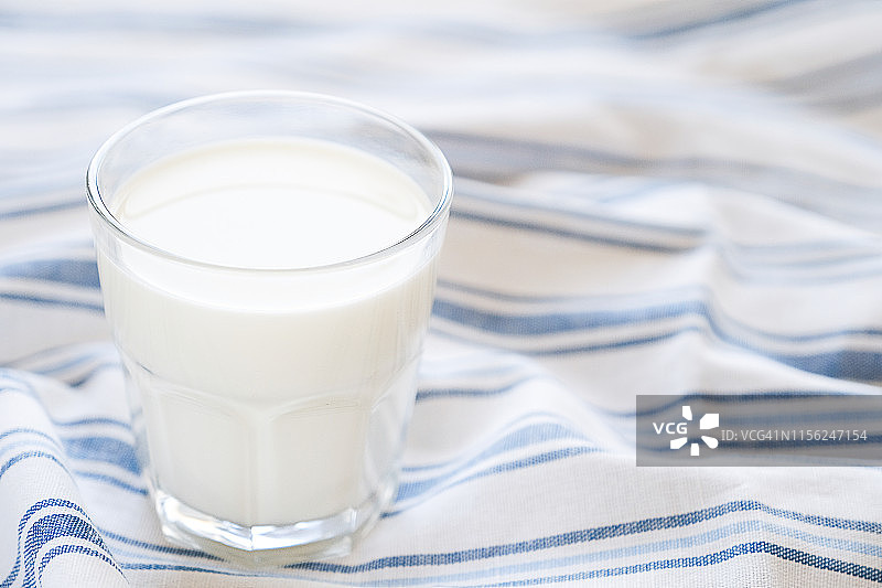 一条带条纹的亚麻毛巾上放着一杯新鲜牛奶，特写镜头。健康有机的理念，农家食品。文本复制空间图片素材