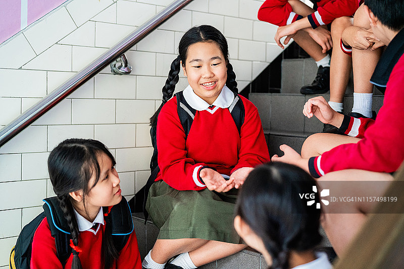 微笑的女学生与朋友在台阶上交谈图片素材
