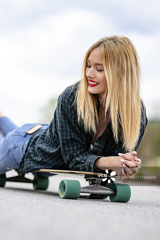年轻女子躺在城市街道的滑板上图片素材