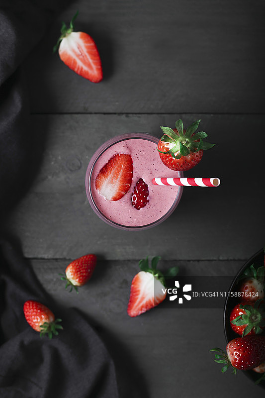 几杯草莓奶昔和草莓放在深色的木头上图片素材