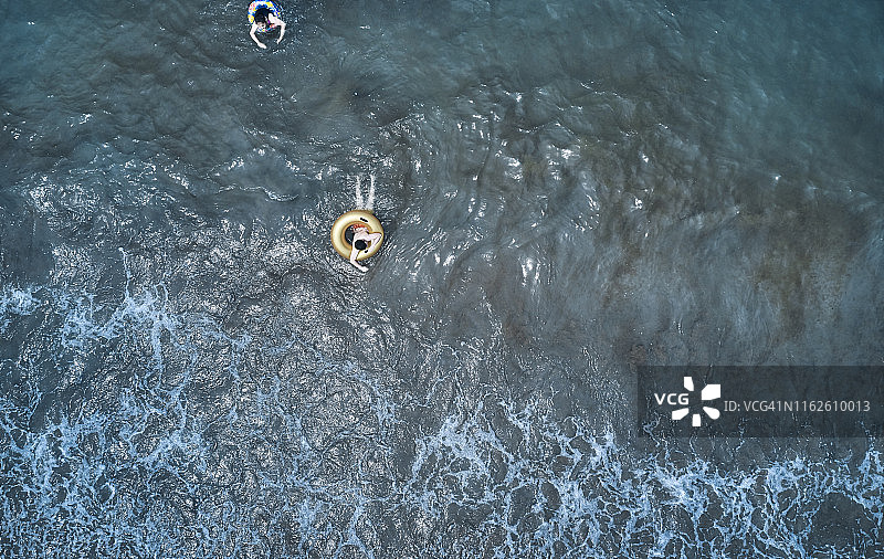 鸟瞰图上的小男孩游泳在黄色游泳环在透明的绿松石海在帕塔拉图片素材