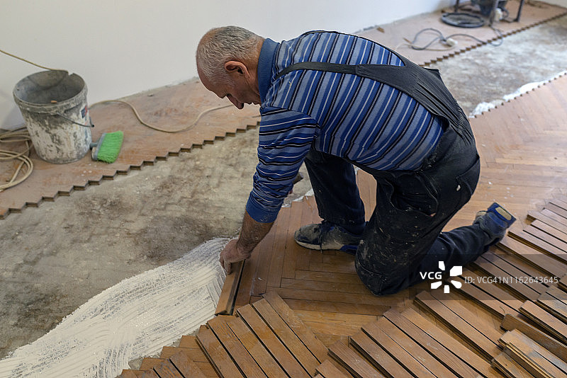 工作中的高级工人正在使用白色胶水安装层压地板或拼花地板图片素材