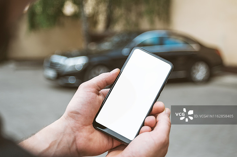 模拟智能手机在一个男人的手中，在背景一辆黑色汽车。图片素材