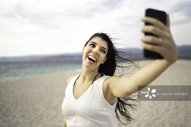 快乐的年轻女子在海滩自拍图片素材
