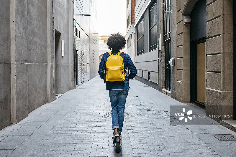在西班牙巴塞罗那的城市里，一个背着黄色背包的年轻人的背影图片素材