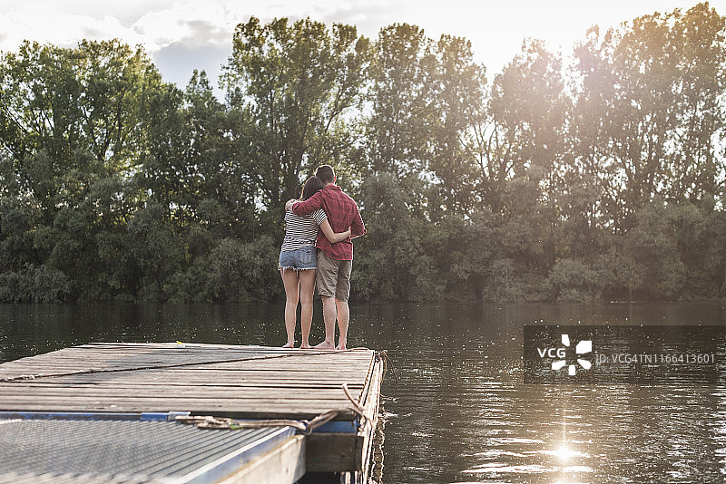 一对年轻夫妇在一个遥远的湖边的码头上拥抱图片素材