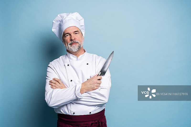 一个成熟的厨师厨师的肖像拿着刀孤立在一个蓝色的背景。图片素材