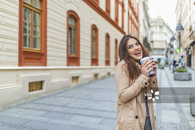 年轻时尚的女人喝着咖啡走在城市的街道上图片素材