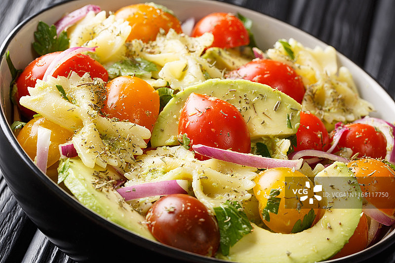 意大利面沙拉与成熟的鳄梨，洋葱和西红柿一起放在一个碗里。水平图片素材