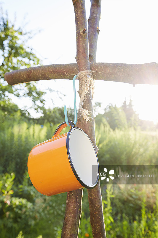 橘色搪瓷杯挂在花园木柱上，户外露营用具图片素材
