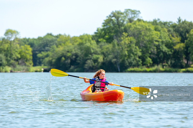 年轻女孩在橙色和黄色皮艇在湖在夏天图片素材