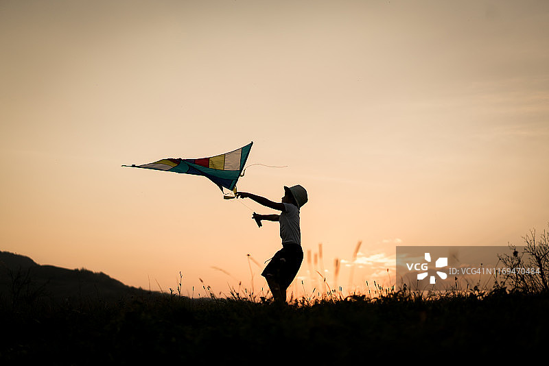 日落时分，草地上孩子拿着风筝的剪影图片素材