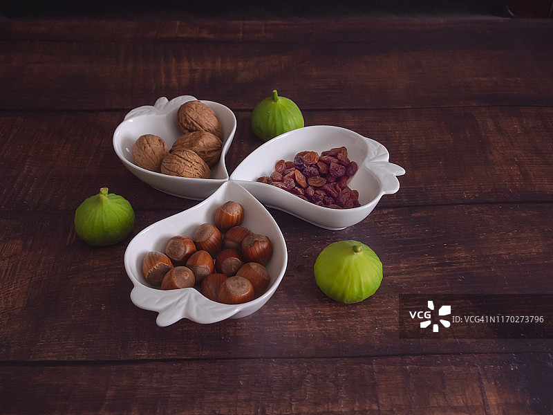 秋天的水果:一堆坚果、榛子、无花果和葡萄干，放在一个旧木桌上的心形瓷碗里图片素材