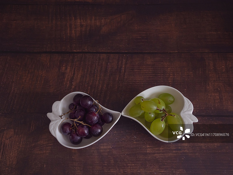 秋天的果实:一串黑葡萄和白葡萄放在一个旧木桌上的心形瓷碗里图片素材