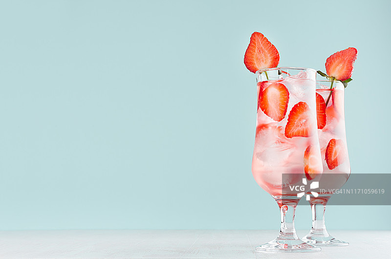 鲜红的水果片，冰块，气泡水在两个雾杯清凉的草莓饮料在现代薄荷颜色内饰。图片素材