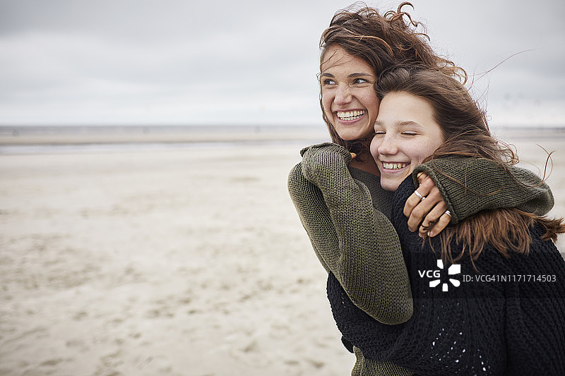 一个快乐的年轻女人在沙滩上拥抱着一个女孩图片素材