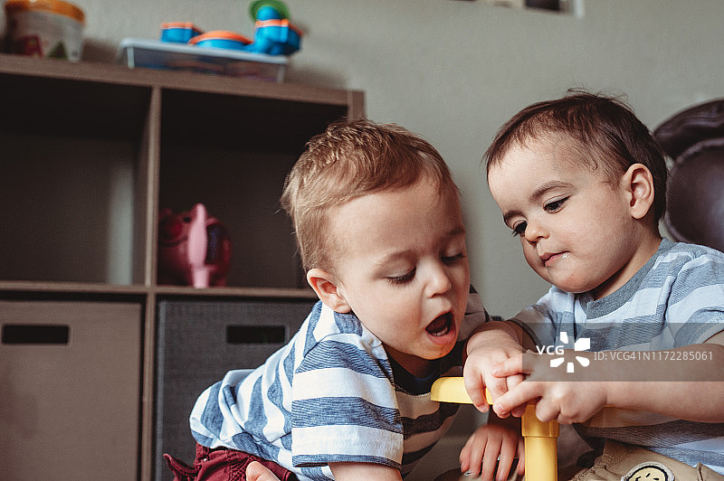 双胞胎男孩在家里的客厅里玩一个老式玩具。图片素材