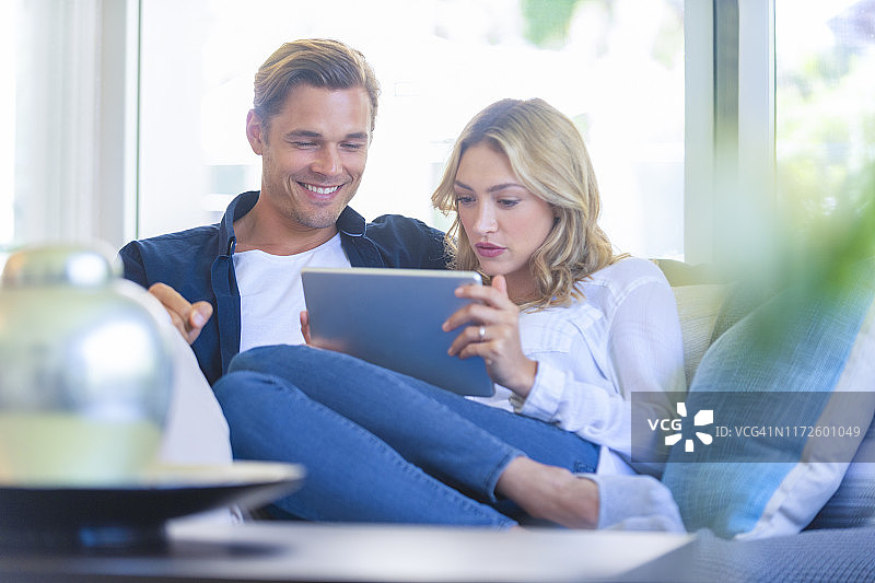 一对幸福的夫妇坐在沙发上看数字平板电脑咖啡。图片素材