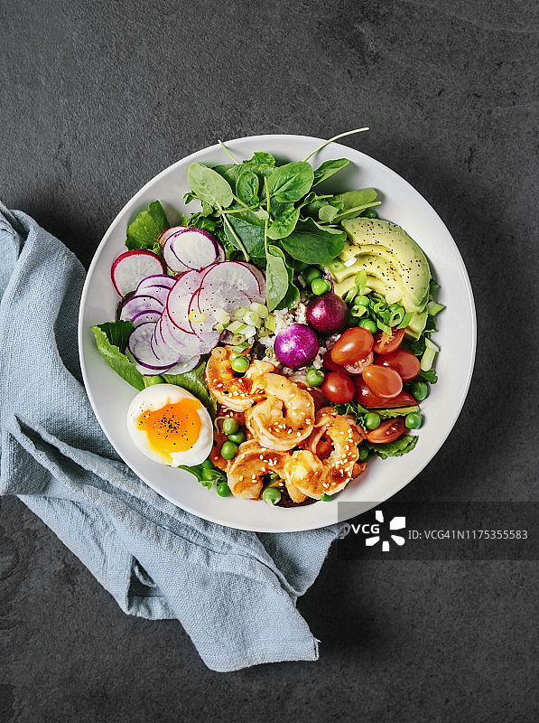 健康的午餐碗，有绿色蔬菜，鳄梨，圣女果，萝卜，水煮鸡蛋和虾在黑色的背景图片素材