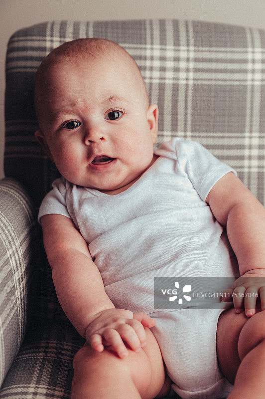 7个月大的男婴穿着白色连体衣坐在格子摇椅和地毯上图片素材
