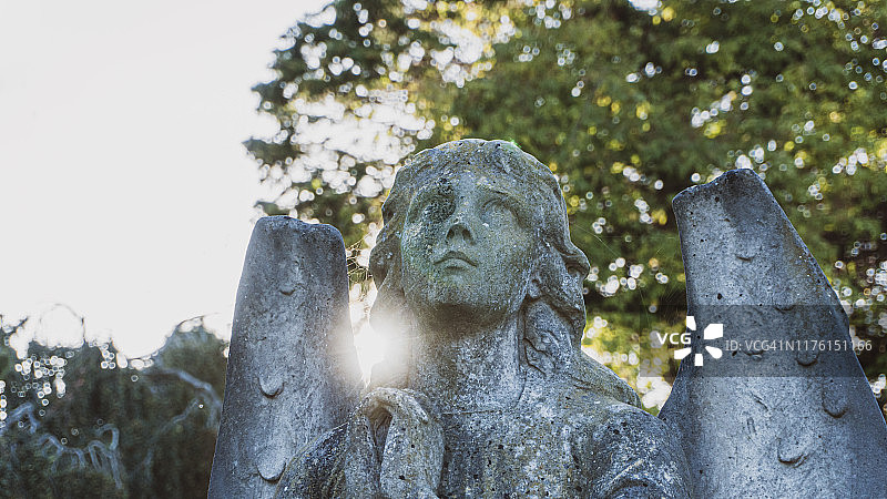 一个女性，石头，墓地天使，握着她的双手祈祷，仰望天空。具有艺术的太阳耀斑和散焦背景图片素材