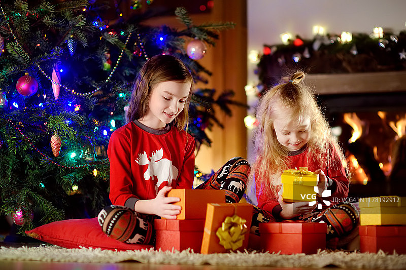 圣诞节前夕，快乐的小妹妹们穿着圣诞睡衣在舒适黑暗的客厅壁炉旁玩耍图片素材