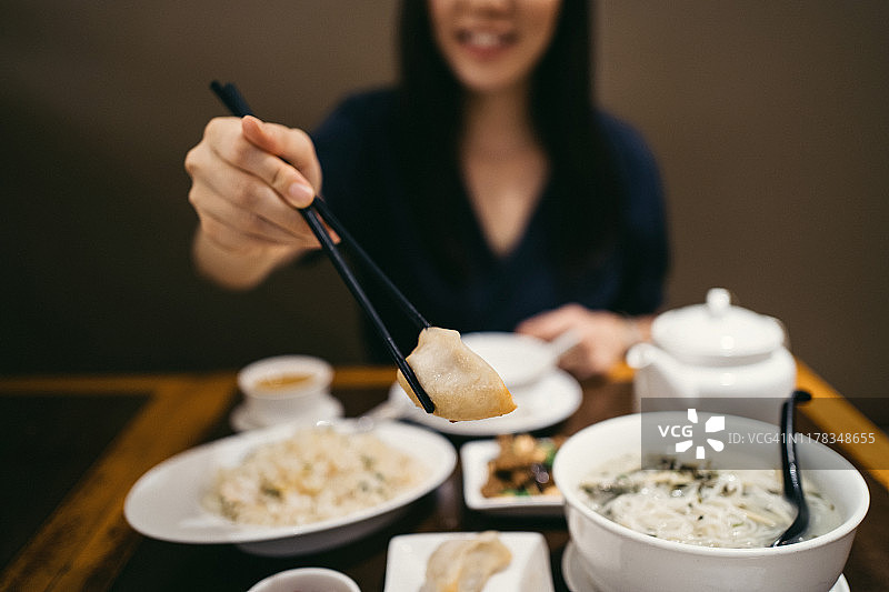 在中国餐馆里，微笑的年轻亚洲妇女正在用筷子吃饺子，享受着各种各样的菜肴图片素材