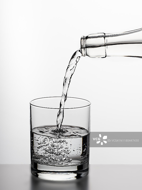 白色背景上的玻璃瓶水装满一个饮用玻璃杯。图片素材