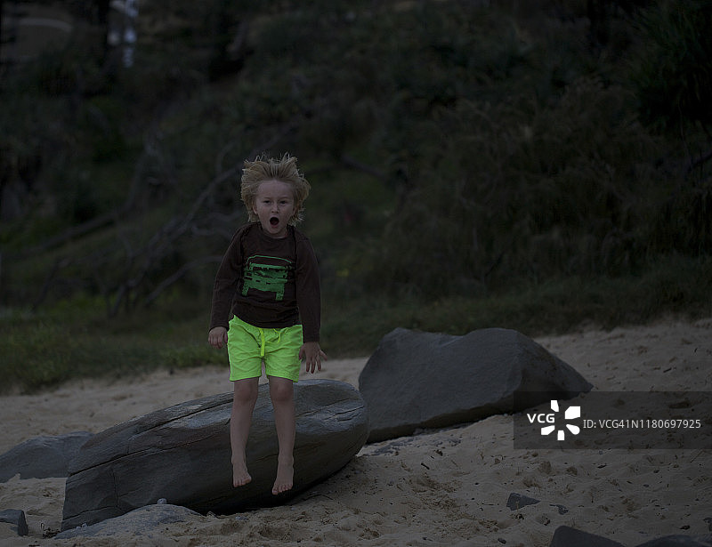 一个4岁的男孩在海滩上从岩石上跳下来图片素材