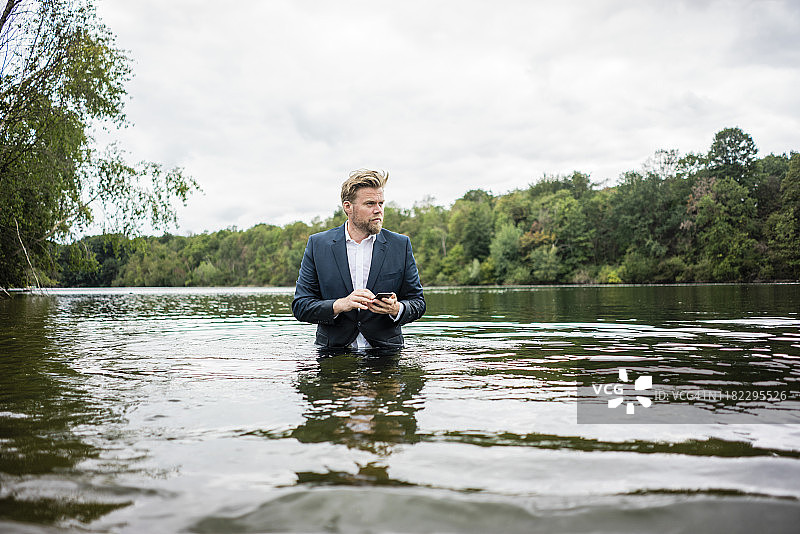 一个商人拿着手机站在湖边图片素材