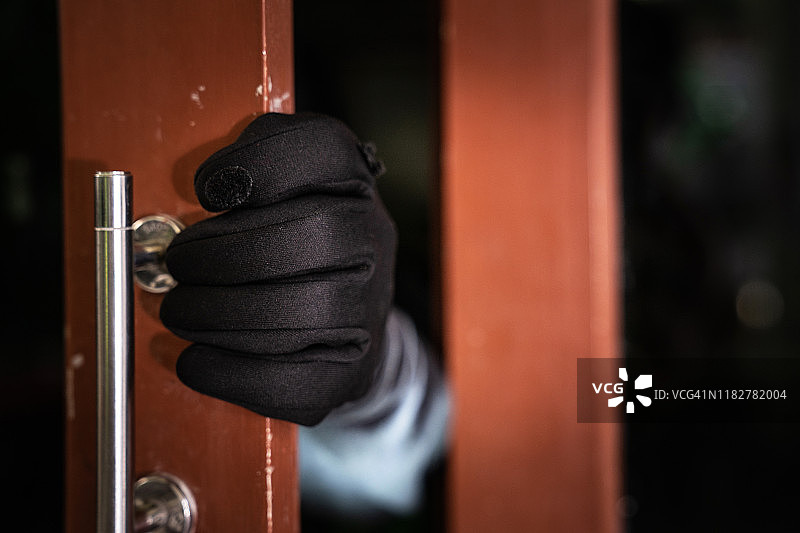 危险的蒙面窃贼拿着撬棍闯入受害者家的门，家庭保险概念图片素材