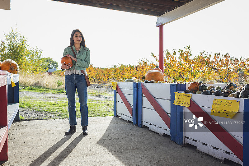 一个年轻女人在秋天的户外水果摊上买南瓜图片素材