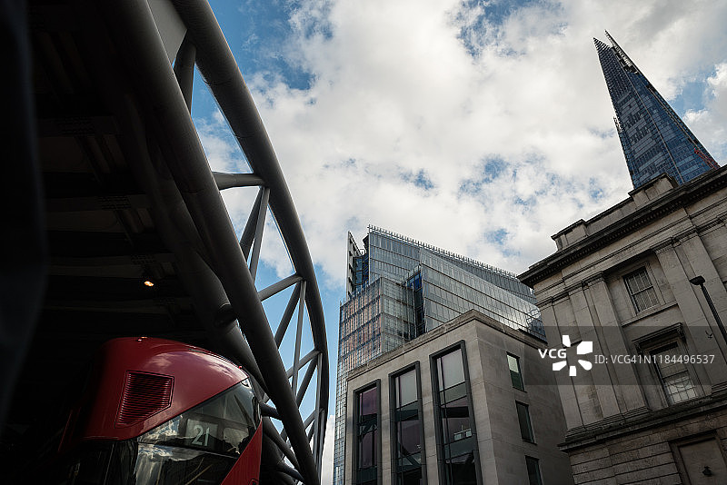 低角度的摩天大楼和一辆红色的公共汽车在伦敦金融区桥下行驶，英国，英国图片素材