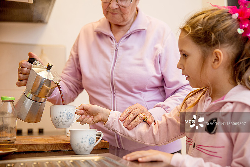 孙女帮奶奶在咖啡杯里倒咖啡图片素材