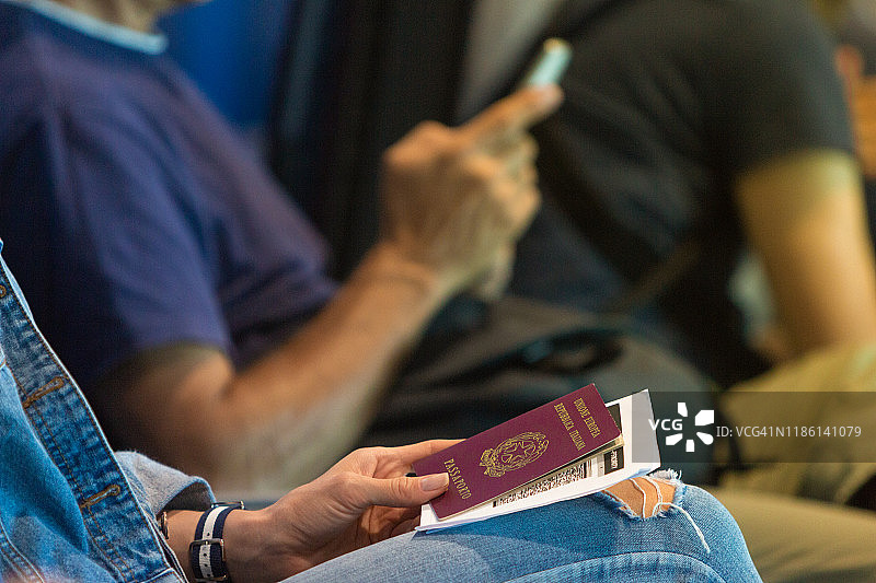 一位女士在机场大厅里等待她的航班，手里拿着护照和登机牌图片素材