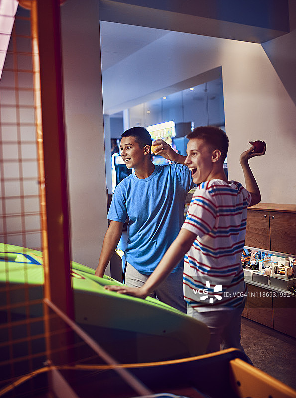 快乐的青少年朋友们在游乐场里向一台游戏机扔球图片素材