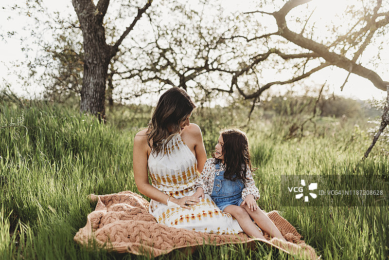 母亲和女儿坐在毛毯上的全长视野图片素材