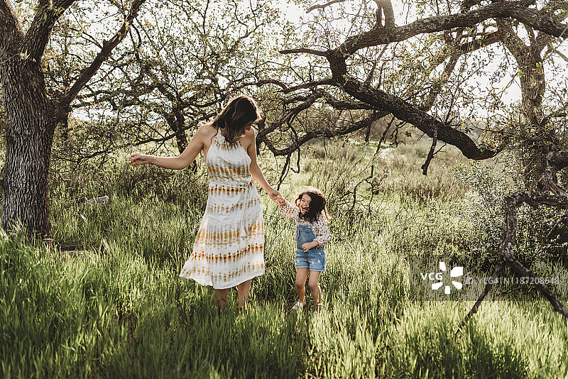 母亲和女儿手牵着手，在背光的草地上跳舞图片素材