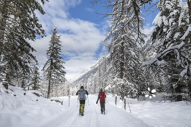 一对徒步旅行者在白雪覆盖的森林小径上散步图片素材