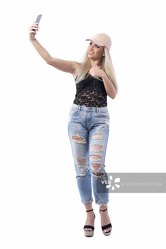 快乐年轻时髦的时尚女孩与帽子自拍，显示像拇指向上的手势图片素材