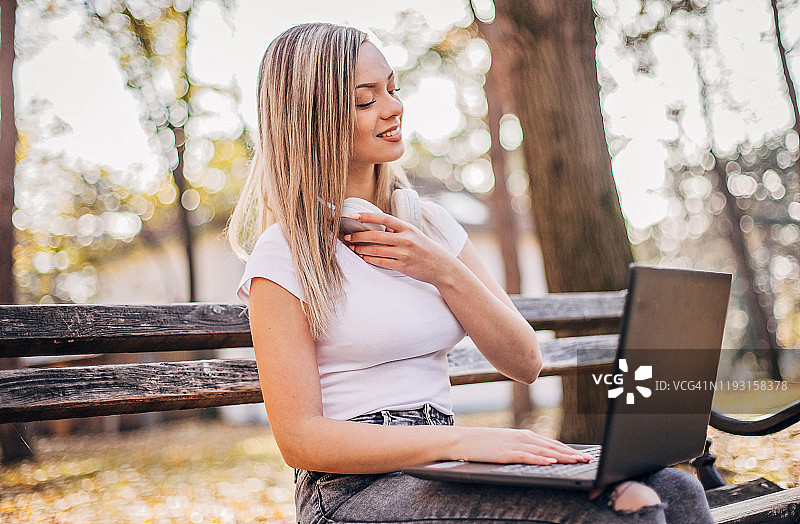 一位年轻女子正坐在公园的长椅上使用笔记本电脑图片素材