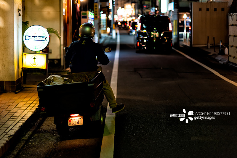 祗园，日本京都晚上与男人在大街上的摩托车送食物图片素材