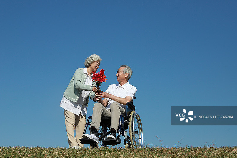 老年妇女给坐在轮椅上的老年男子送花图片素材