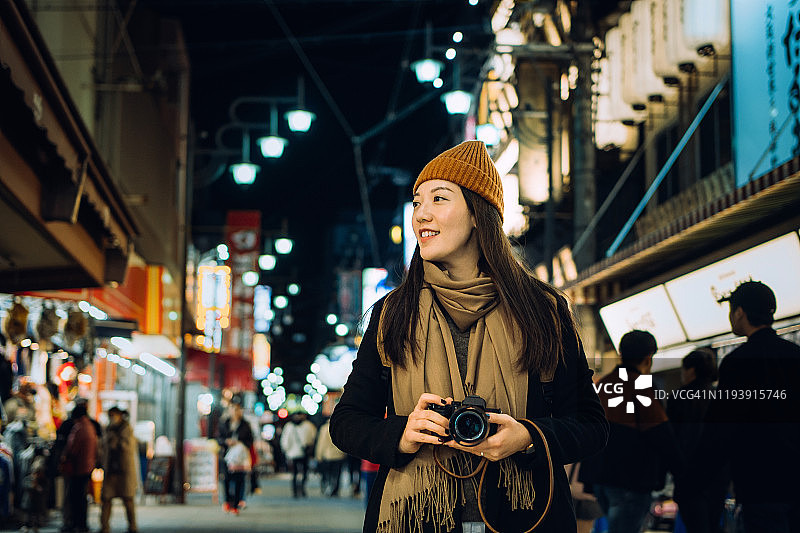 在日本大阪，年轻的亚洲女游客带着相机，在当地繁忙的街道上漫步图片素材