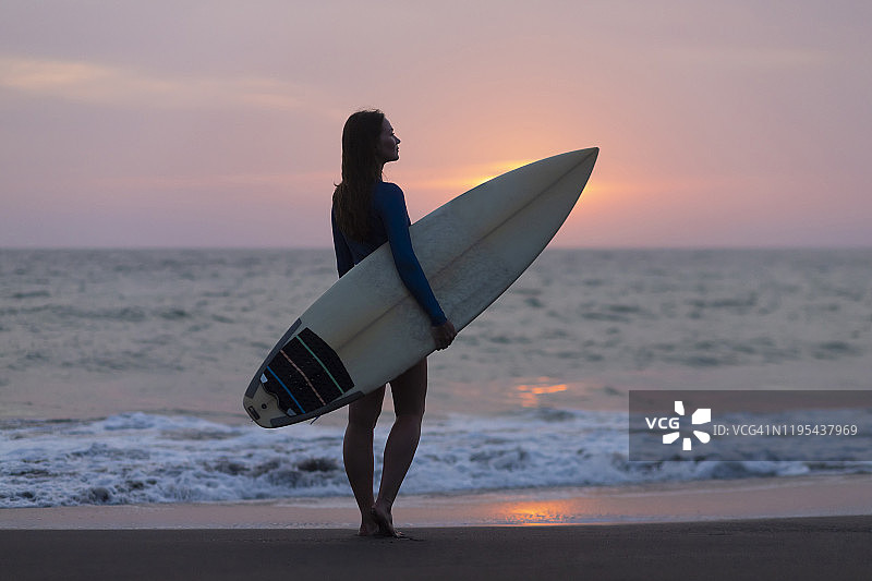 年轻女子与冲浪板在海滩上，克顿古海滩，印度尼西亚巴厘岛图片素材