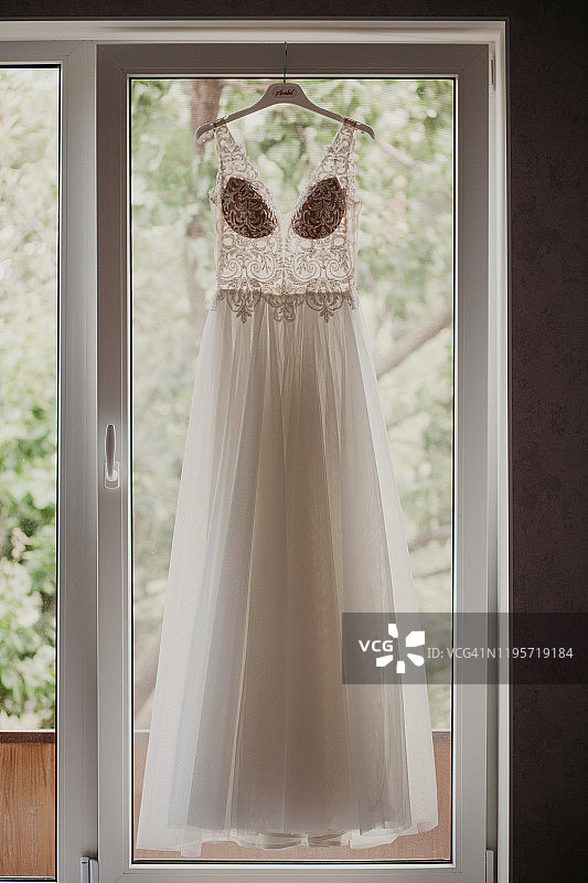 婚纱挂在新娘房靠近窗户的衣架上。在她的婚礼上图片素材
