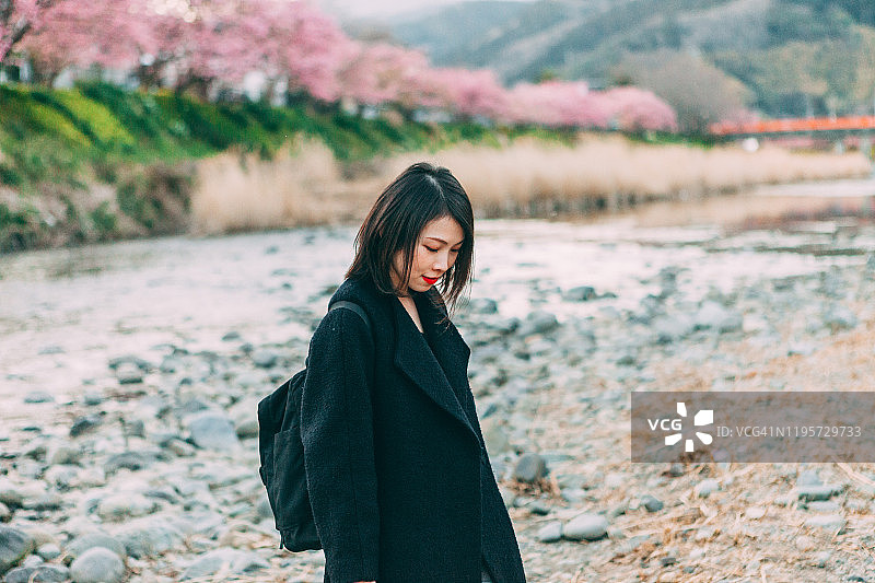 美丽开朗的年轻女子沿着河边散步，背景是日本樱花图片素材