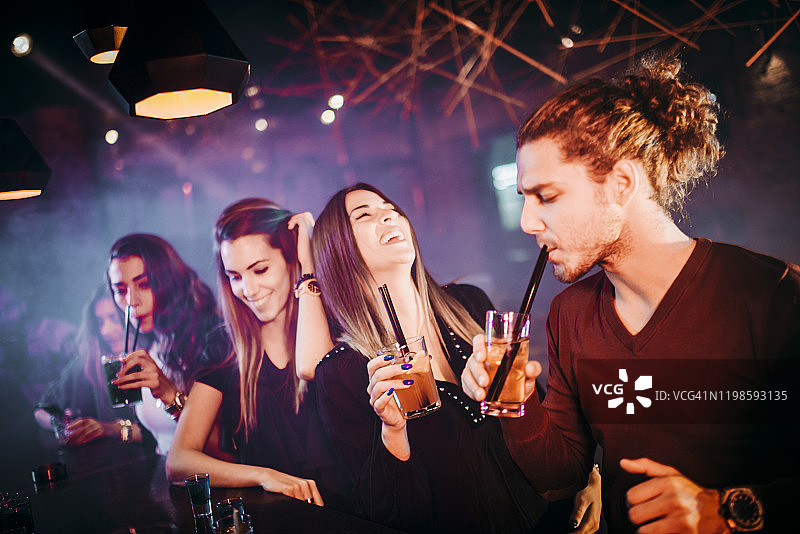 一个年轻人和他的两个女性朋友在一个俱乐部的鸡尾酒之夜享受鸡尾酒图片素材