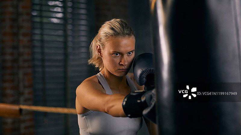 水平肖像强壮的女人打击沉重的袋子在拳击训练图片素材