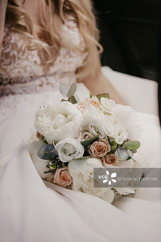 新娘手捧婚礼花束。美丽的新娘坐在和拿着婚礼花束美丽的玫瑰和樱桃。穿着白色的连衣裙和漂亮的锁扣。近距离图片素材